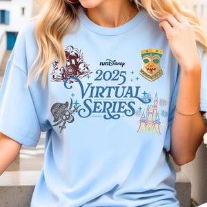 May include: Light blue t-shirt featuring the text "runDisney 2025 Virtual Series" with various graphics. Graphics include a train, a tiki, a pirate skull, and a castle. The shirt is short-sleeved.