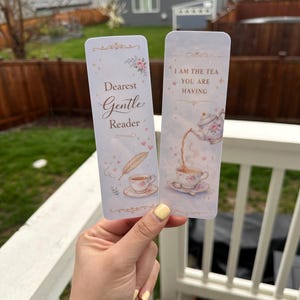 May include: Two decorative bookmarks with floral and tea cup illustrations. One bookmark reads "Dearest Gentle Reader" and the other says "I AM THE TEA YOU ARE HAVING". The bookmarks have a light blue background with pink and gold accents.