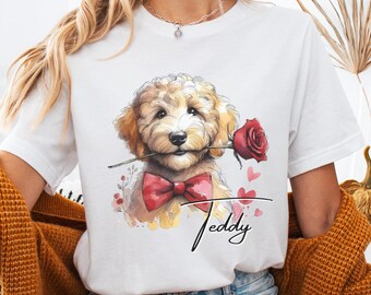 Può includere: Maglietta bianca con un'illustrazione ad acquerello di un cane che tiene una rosa rossa in bocca. Il cane indossa un papillon rosso e il testo "Teddy" è scritto sotto il cane.