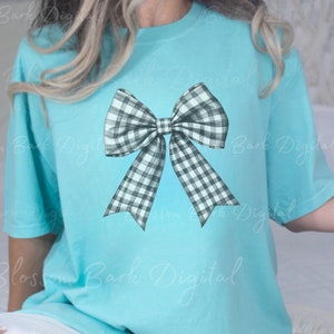 Puede incluir: Una camiseta azul claro con un dise&ntilde;o de lazo a cuadros en blanco y negro.