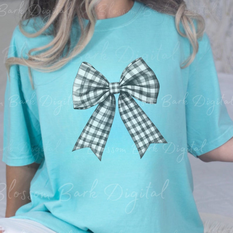 Puede incluir: Una camiseta azul claro con un dise&ntilde;o de lazo a cuadros en blanco y negro.