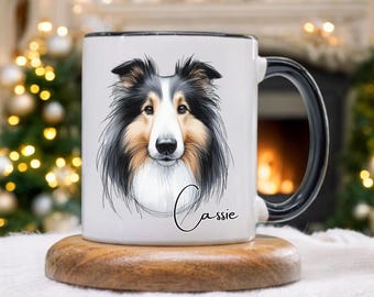 Könnte beinhalten: Weiße Keramiktasse mit einer detaillierten Illustration des Gesichts eines Collie-Hundes mit schwarzem und braunem Fell. Die Tasse hat einen schwarzen Rand und Henkel, und der Name "Cassie" ist in Schreibschrift geschrieben. Die Tasse steht auf einem Holzuntersetzer.