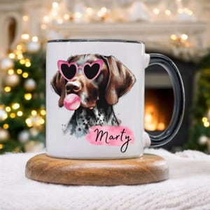 May include: White ceramic mug with a black handle and rim, featuring a dog wearing pink heart-shaped sunglasses and blowing a bubble. The dog's name, "Marty," is written in cursive on a pink watercolor-style background.