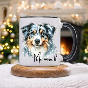 May include: White ceramic mug with a black handle and rim, featuring a detailed illustration of a dog with blue eyes and a multi-coloured coat. The name "Maverick" is written in cursive below the dog's image. The mug sits on a wooden coaster.