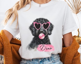 May include: White t-shirt featuring a black dog wearing pink heart-shaped sunglasses and blowing a bubble. The dog's name, "Dino," is written in cursive on a pink banner below the dog.