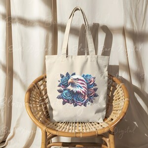 May include: A white canvas tote bag with a blue, red, and white American flag eagle design surrounded by blue roses. The eagle's head is facing the left side of the bag.