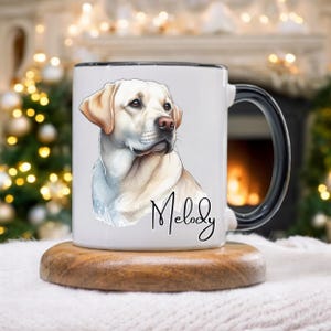 May include: White ceramic mug with a black handle and rim, featuring a watercolor illustration of a yellow Labrador Retriever. The dog's name, "Melody," is written in cursive below the image. The mug sits on a wooden coaster.