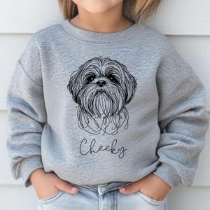 Könnte beinhalten: Ein graues Sweatshirt mit einer schwarzen Linienzeichnung eines Shih Tzu-Hundegesichts und dem darunter gedruckten Wort "Cheeky".