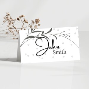 May include: White place card with a gray floral design and gray hearts. The name "John Smith" is written in black cursive.
