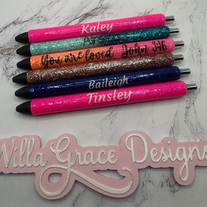 May include: A set of seven glitter pens with personalized names and messages. The pens are pink, teal, orange, brown, navy blue, and black. The text on the pens reads: Kaley, Ana, You are loved, Forever, John 3:16, Baiteigh, and Tinsley.