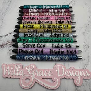 May include: A set of 12 glitter pens with bible verses printed on them. The pens are in various colors, including blue, pink, green, and gold. The pens are arranged vertically, with the writing facing the viewer. The pens are all capped and have silver metal tips. The text on the pens includes verses such as "Hope Hebrews 6:19", "Believe John 3:16", "Faith Hebrews 11", "Love One Another 1 John 4:7", "Jesus is the way Luke 14:6", "Peace Philippians 4:7", "Obey John 14:23", "Trust God John 19:1", "Pray 1 Thessalonians 5:17", "Serve God Luke 4:8", "Praise God Psalm 106:1", and "Forgive 1 John 19".