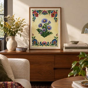 May include: A framed rectangular print featuring a central cluster of purple aster flowers on a pale yellow background, surrounded by a decorative border of colourful floral motifs in shades of red, blue, green, and yellow, encased in a wood frame.