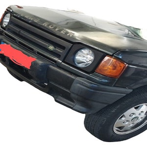 Pode incluir: Um Land Rover Discovery preto com uma grelha preta e um emblema LAND ROVER prateado. O pára-choques dianteiro é preto e os faróis estão ligados.