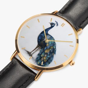 May include: Gold-tone wristwatch with a black leather band. The watch face features a watercolor painting of a peacock in shades of blue, gold, and teal. The watch has gold hands and hour markers.