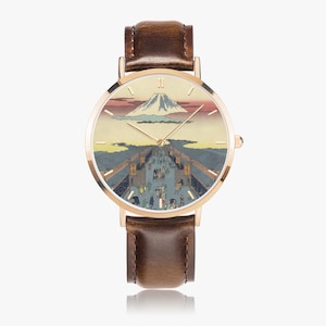 May include: A rose gold wristwatch with a brown leather band. The watch face features a Japanese landscape painting with a mountain, people, and buildings. The watch has gold hands and a gold bezel.