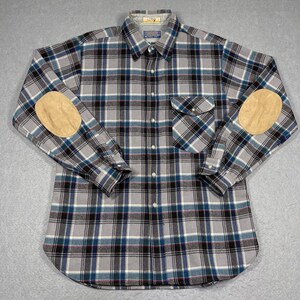May include: A long-sleeved flannel shirt with a gray, blue, and black plaid pattern. The shirt has two suede elbow patches and a single chest pocket.