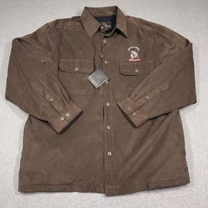 May include: A brown suede long-sleeve button-up shirt with two chest pockets and a Native American headdress logo that says "Proud U.S. Veteran".