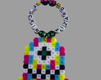 May include: A colourful beaded charm with the words "F*CKIN WIZARD" and a smiley face. The charm is attached to a pixelated ghost-shaped charm with black, white, yellow, pink, blue and green beads.