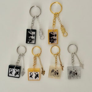 Peut inclure: Ensemble de six porte-clés avec des designs différents. Chaque porte-clés présente un petit cadre photo rectangulaire avec une image en noir et blanc de deux personnes. Les porte-clés sont attachés à des chaînes argentées et dorées avec différents breloques.