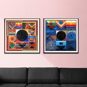 May include: Two framed abstract paintings with geometric shapes and a black circle in the center. The painting on the left has a red, yellow, and blue color scheme. The painting on the right has a blue, green, and yellow color scheme. The paintings are hung on a pink wall.