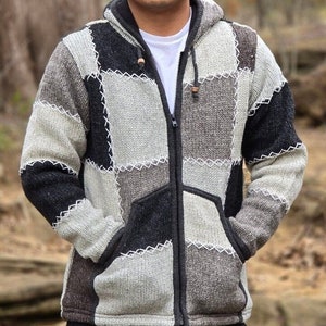 Puede incluir: Un suéter con capucha gris y negro de patchwork con cierre de cremallera. El suéter está hecho de una tela suave y tejida y tiene un ajuste holgado.