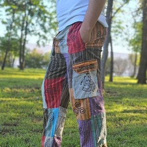 Op de afbeelding: Veelkleurige patchwork broek met geborduurde symbolen en een gestreept patroon. De broek heeft een grote cargozak op het rechterbeen.