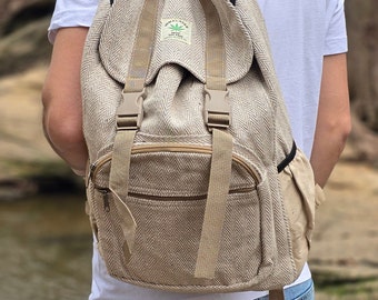 Op de afbeelding: Een beige hennep rugzak met een bruine rits en verstelbare banden. De rugzak heeft een klein groen blaadjeslogo met de tekst "Hemptique" en "Home Grown Textiles" erop.