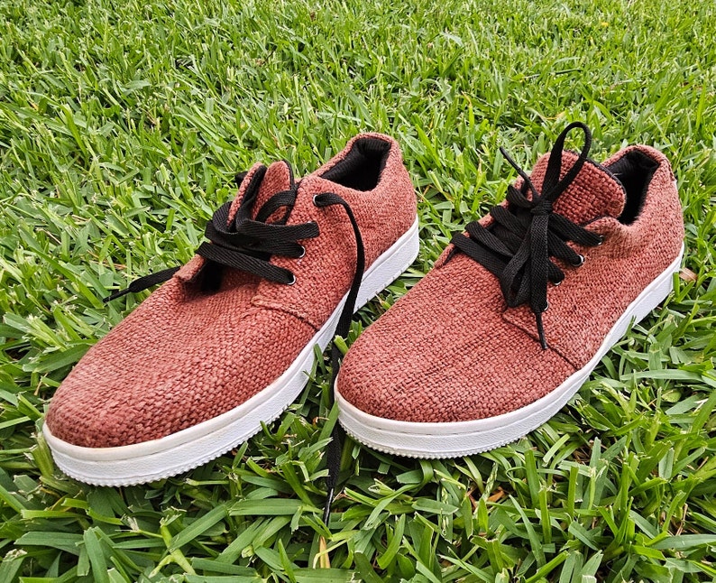 Pode incluir: Um par de sapatos de lona marrons com cadar&ccedil;os pretos. Os sapatos t&ecirc;m uma sola branca e s&atilde;o feitos de um tecido texturizado.