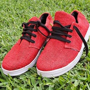 Pode incluir: Um par de sapatos de lona vermelhos com cadar&ccedil;os pretos. Os sapatos t&ecirc;m solas brancas e s&atilde;o feitos de um tecido texturizado.