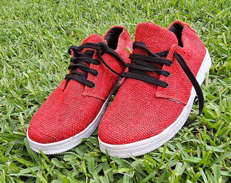 Pode incluir: Um par de sapatos de lona vermelhos com cadar&ccedil;os pretos. Os sapatos t&ecirc;m solas brancas e s&atilde;o feitos de um tecido texturizado.