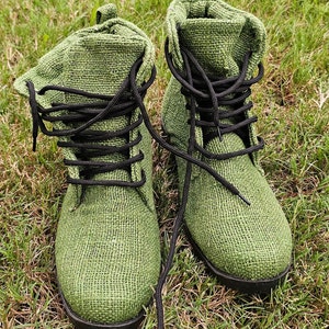 Pode incluir: Um par de botas de lona verde com cadar&ccedil;os pretos. As botas est&atilde;o sobre um leito de grama verde.