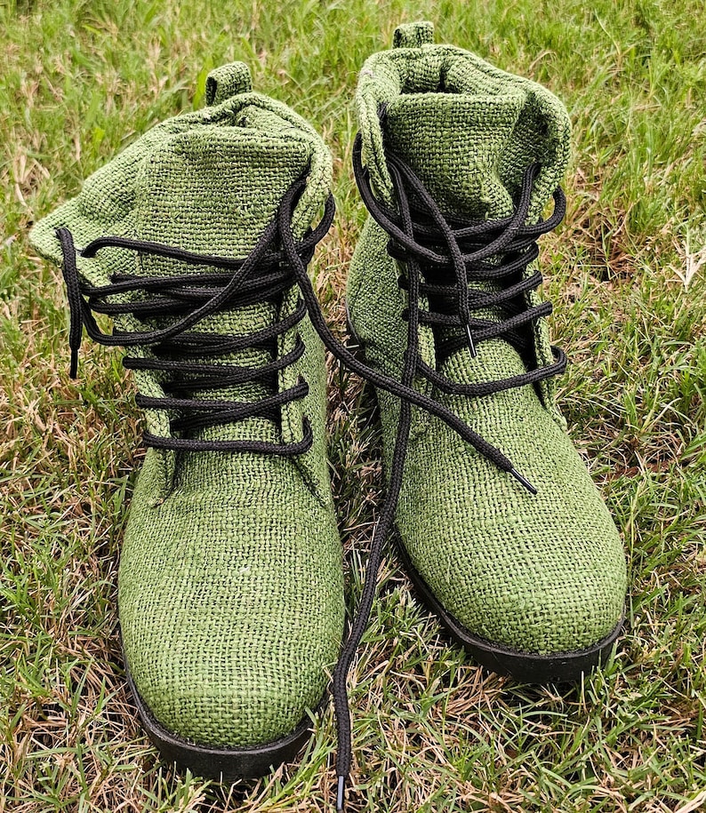 Pode incluir: Um par de botas de lona verde com cadar&ccedil;os pretos. As botas est&atilde;o sobre um leito de grama verde.