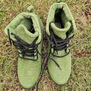 Pode incluir: Um par de botas de lona verde com cadar&ccedil;os pretos. As botas est&atilde;o sobre um leito de grama verde.