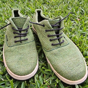 Pode incluir: Um par de sapatos de lona verde com cadar&ccedil;os pretos. Os sapatos t&ecirc;m uma sola branca e s&atilde;o feitos de um tecido tecido.