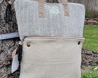 May include: A black and white chevron patterned hemp tote bag with a beige diamond patterned bottom section. The bag has a brown leather handle and a brown leather zipper. The bag has a small black tassel on the side. The bag has a label that says "GANAMO, 100% HEMP, NATURAL FIBRE".
