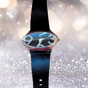 Könnte beinhalten: Schwarze Lederarmbanduhr mit ovalem Zifferblatt. Das Zifferblatt ist schwarz mit großen weißen Ziffern und dem Wort "STORM". Die Uhr hat eine silberne Lünette mit rosa Akzent.