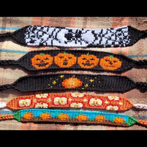 May include: Five colorful friendship bracelets with various pumpkin and Halloween-themed designs. The bracelets are made with colorful embroidery floss and feature black, white, orange, red, blue, and green colors.