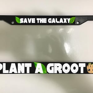May include: Black license plate frame with white text that reads "SAVE THE GALAXY" and "PLANT A GROOT". The frame has green leaf accents and a Groot character graphic.