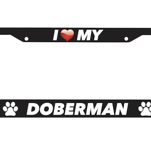 Puede incluir: Marco de matrícula negro con texto blanco que dice "Amo a mi Doberman" con un corazón rojo y huellas de patas a cada lado.