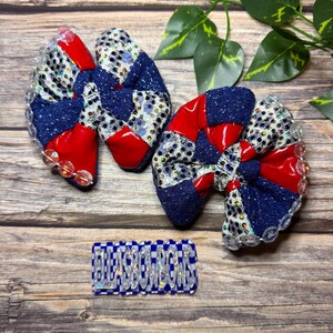 May include: Two handmade hair bows with red, navy blue, and silver accents. The bows have a patchwork design and are embellished with clear beads. A small rectangular tag with the text "BLESSBOWS" is also present.