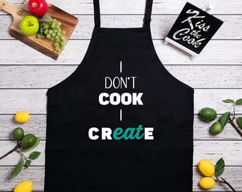 May include: Black kitchen apron with white text that reads "I don't cook I create" in a teal green font.