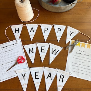 May include: A festive New Year banner with the words "HAPPY NEW YEAR" printed on triangular flags. The banner is accompanied by a spool of twine, scissors, and devotional materials. A decorative tray with a small tree is in the background.