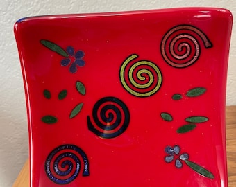 Captivating red fused glass plate/tray with metallic spirals and glass flower pattern. Backside is multicolored glass. 6x6 inches.