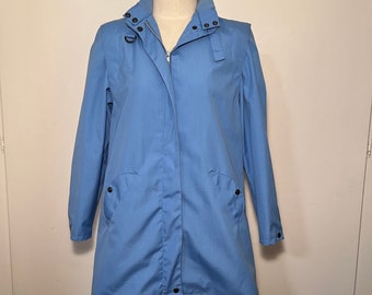 May include: A light blue raincoat with a zipper closure and a stand-up collar. The raincoat has two pockets and a button at the bottom.