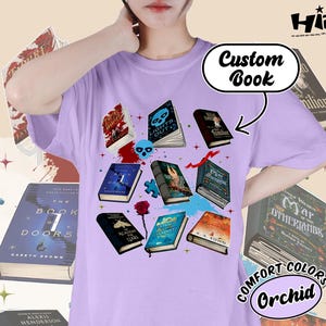 May include: Orchid-colored t-shirt featuring a graphic of several open books with various covers, including "Lights Out" and "The Book of Doors." The design includes a skull, a rose, and the text "Custom Book."