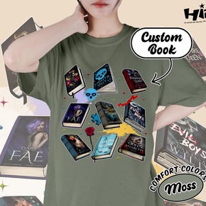 May include: Moss green t-shirt featuring a graphic of various open books with fantasy-themed covers. The words "Custom Book" are above the graphic. The shirt also has the words "COMFORT COLORS" and "Moss" printed on it.