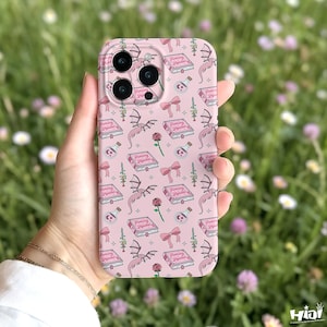 May include: Pink phone case with a repeating pattern of books, dragons, roses, bows, and potion bottles. The book has the text "Fucking Reader". The case has a camera cutout and is held in a hand.