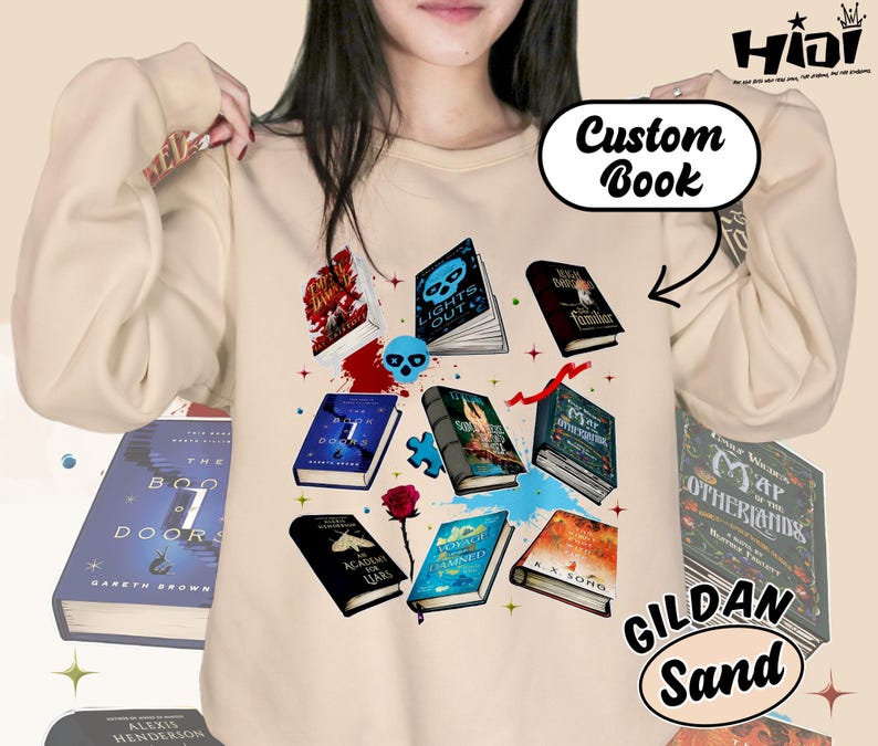 May include: Sand-colored sweatshirt with a graphic of various books, a skull, and a rose. The text "Custom Book" is above the design. The sweatshirt is a Gildan brand.