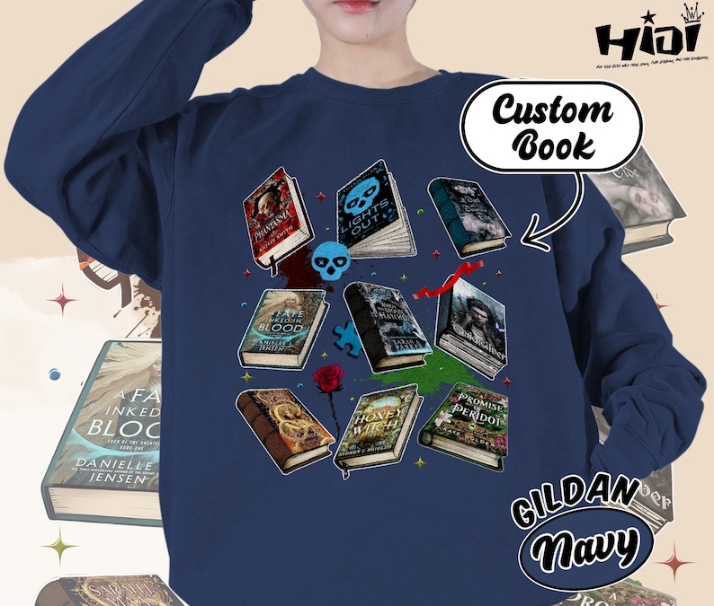 May include: Navy blue sweatshirt featuring a collection of illustrated books with titles like "Lights Out" and "Promise Peridot." The design includes a skull, a rose, and the text "Custom Book." The sweatshirt is labeled "GILDAN Navy."