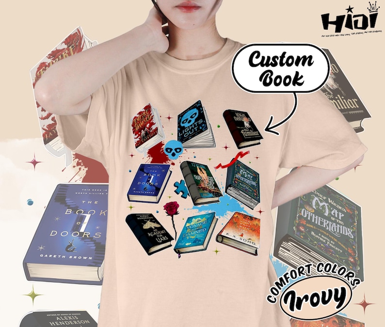 May include: Beige t-shirt featuring a collection of illustrated books with various covers, including titles like "Lights Out" and "The Book of 7 Doors." The design includes a skull, a rose, and the text "Custom Book."